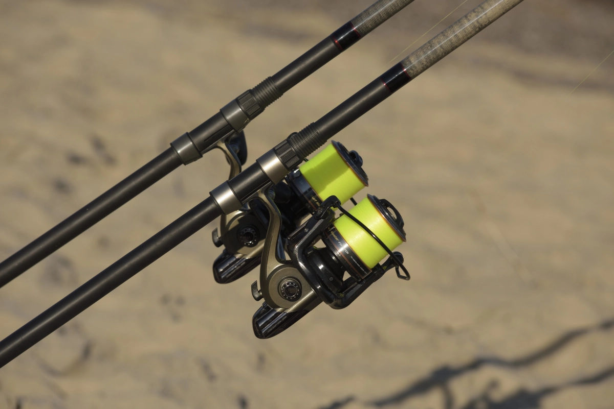 Dwie wędki z kołowrotkami o stałej szpuli na tle piaszczystej plaży