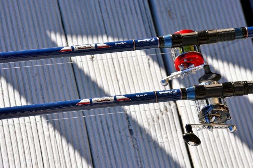 Dwie wędki plażowe Sportex z kołowrotkami na tle pomalowanych na niebiesko ryflowanych desek
