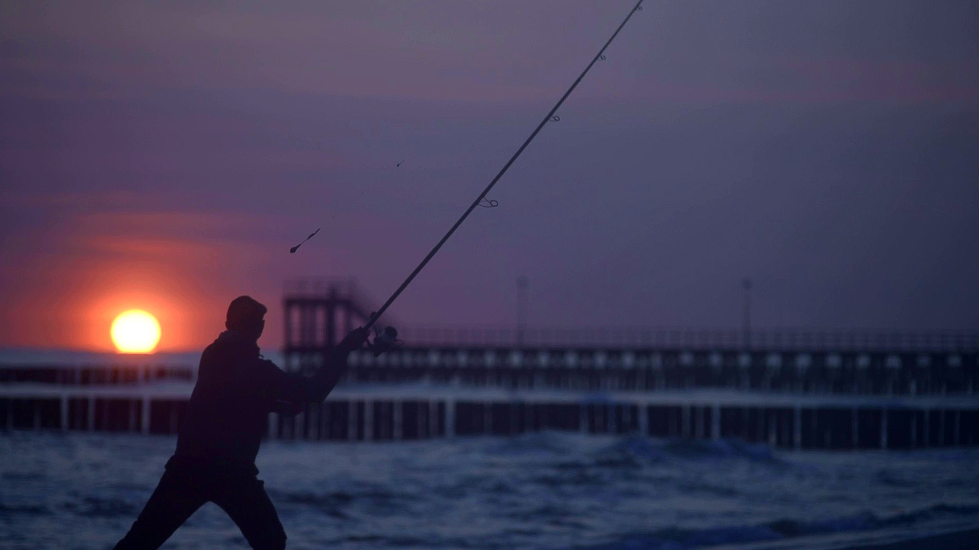 wędkarz stojący w morzu holujący rybę w dużych falach