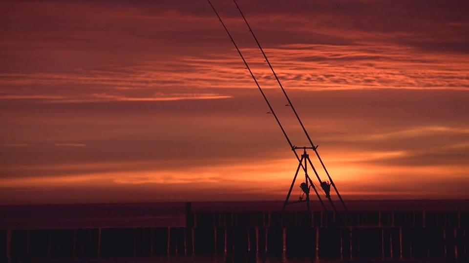 Fotografia ukazująca wędki do surfcastingu na tle wschodu słońca