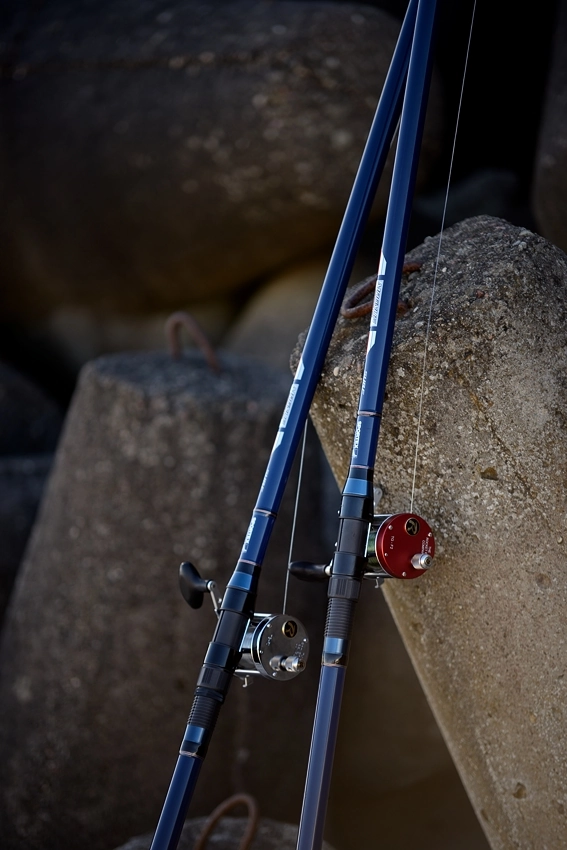 Dwa kołowrotki do wędkarstwa plażowego z niebieskimi wędkami na betonowych blokach ochrony wybrzeża